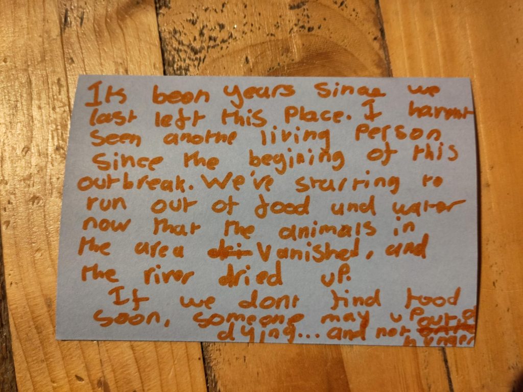 The image represents a creative writing piece written by a young person at a participation session, orange writing on white paper. It reads "It's been years since we last left this place. I haven't seen another living person since the beginning of this outbreak. We're starting to run out of food and water now that the animals in the area vanished, and the river dried up. If we don't find food soon, someone may [end] up dying... and not out of hunger."
